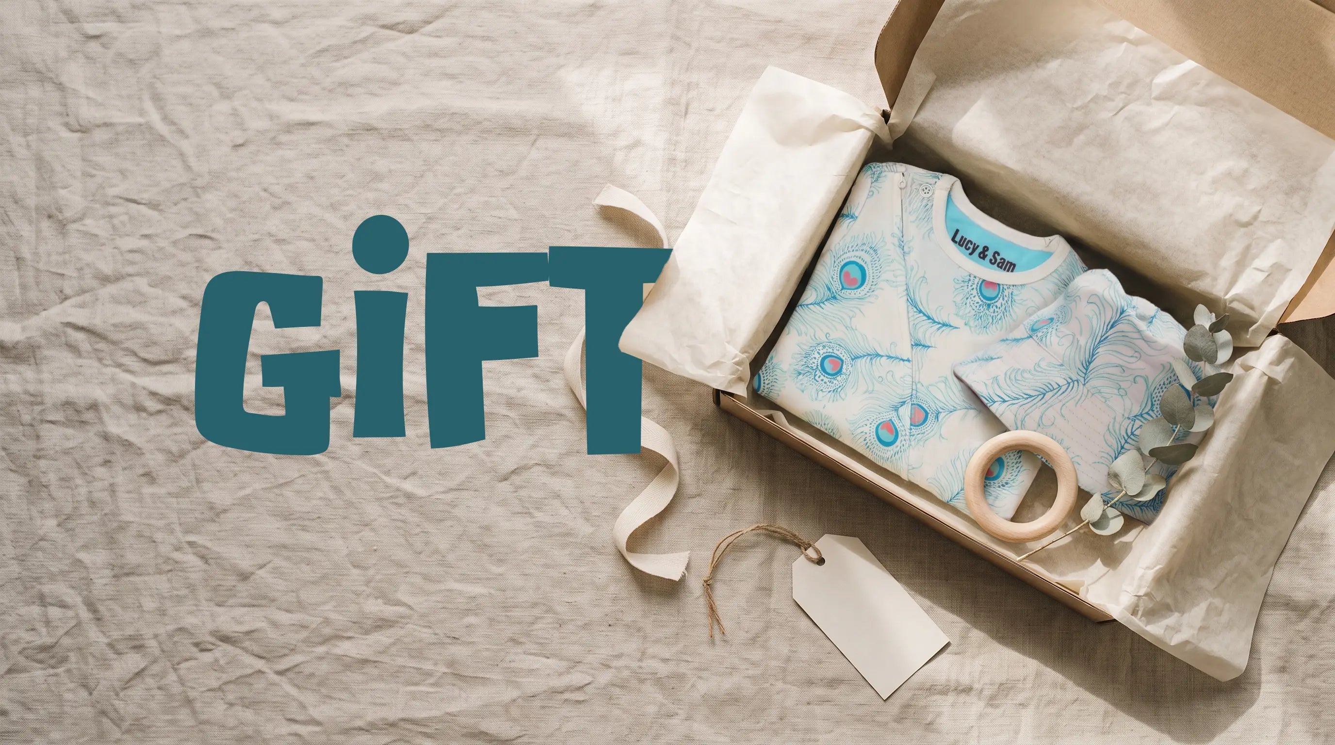 peacock print organic cotton baby sleepsuit in a kraft gift box with a wooden teether, a gender-neutral baby shower gift