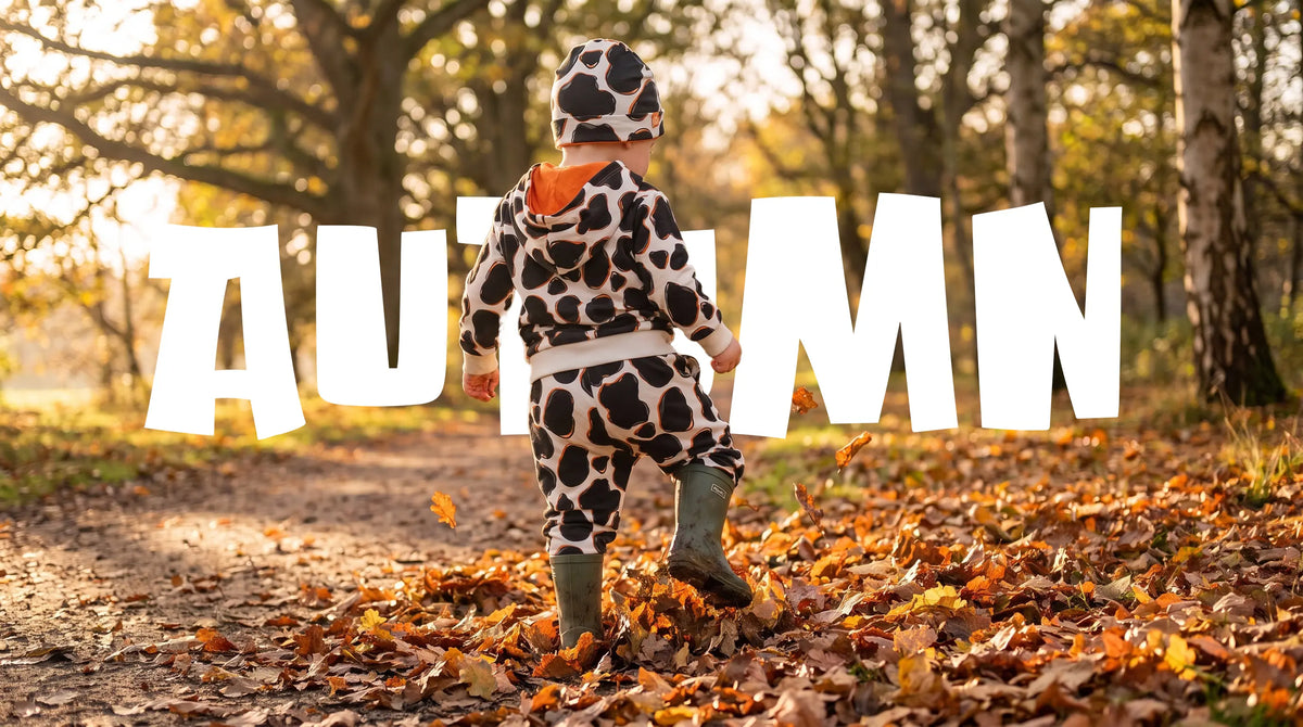 toddler in a cow print organic cotton hoodie, joggers and wellies walking through autumn leaves