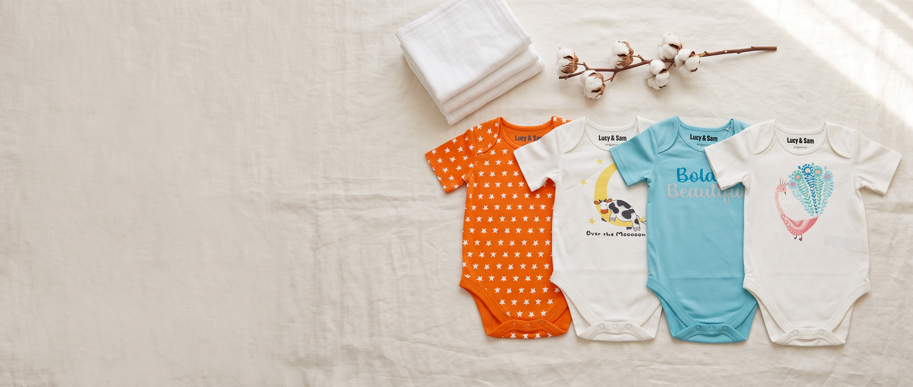 Star & Moon Cow and Bold & Beautiful organic cotton baby bodysuits laid flat on linen